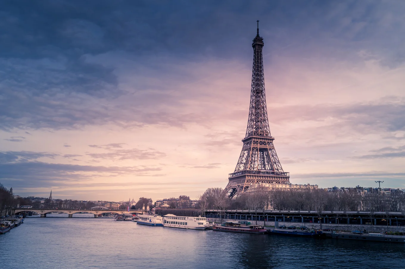Eiffel Tower, river, bridge, boats, cloudy sky.
