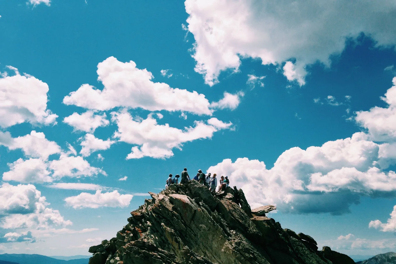 Group on mountain peak, blue sky, white clouds.